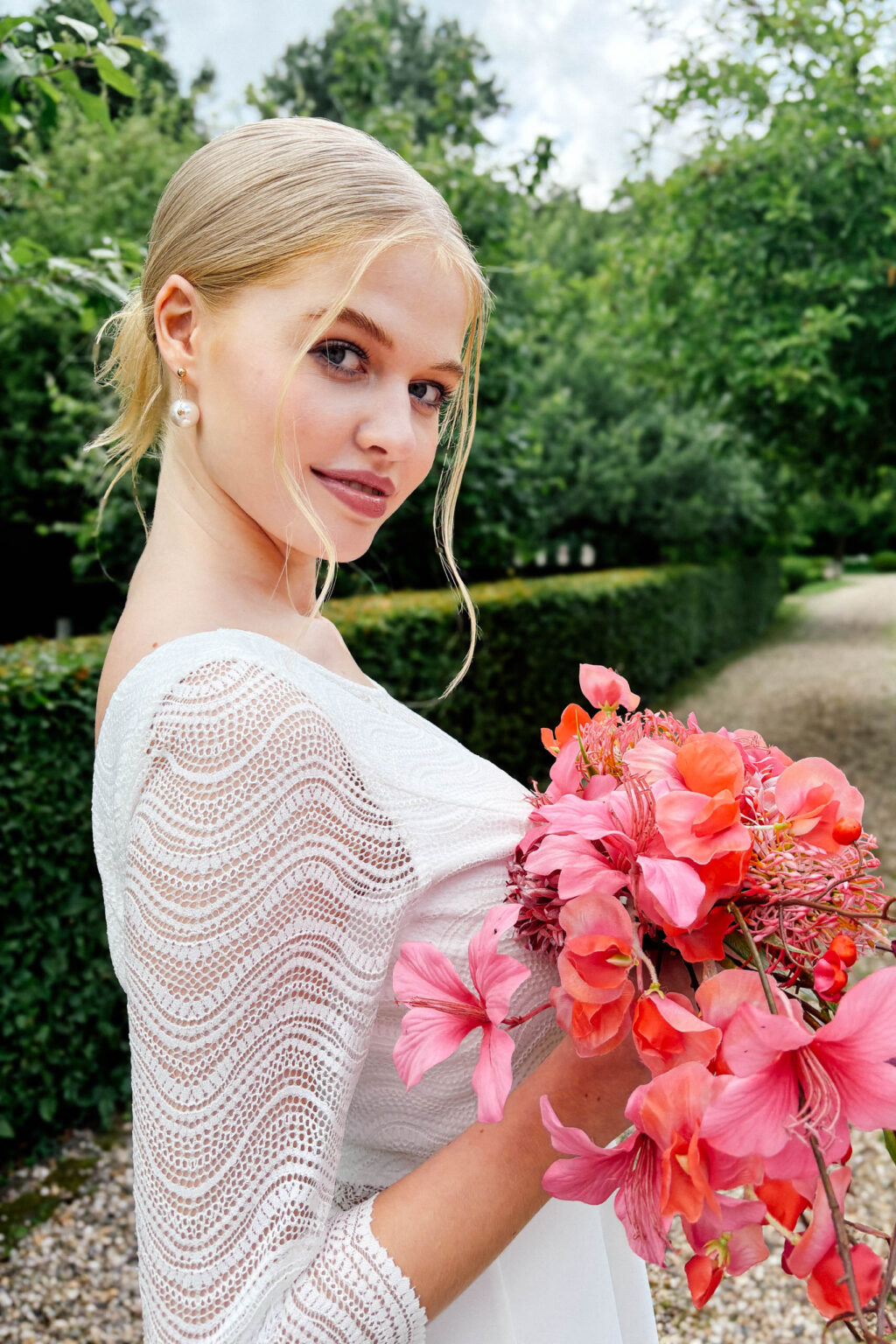 Ärmel aus recycelter Wellenspitze am Brautkleid KUESSdieBOBIGNY mit pinkem Brautstrauß