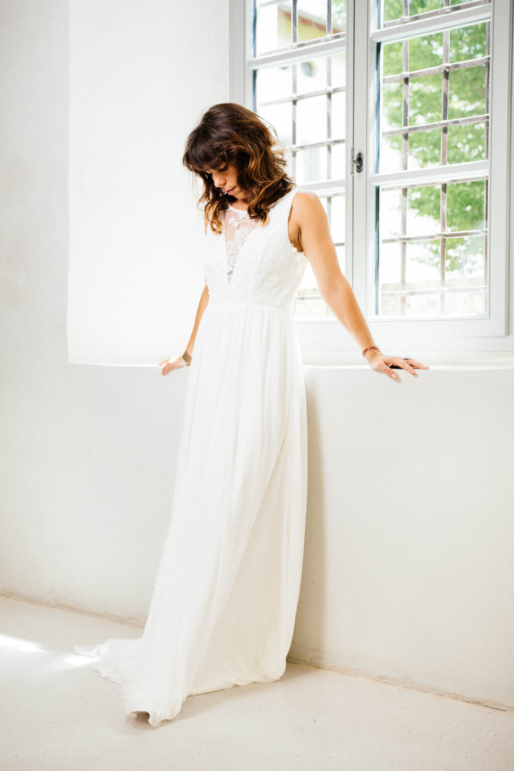 Brautkleid KUESSdieBIBBONA mit glitzerndem 3D-Spitzenoberteil, tiefem V-Ausschnitt und Chiffonrock am Fenster