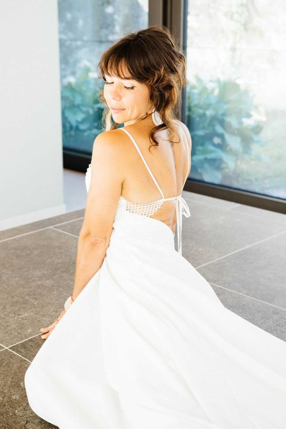 Braut im Boho Brautkleid KUESSdieAGIRA mit Spaghettiträgern und offenem Rücken, Rückenansicht in einem hellen Raum